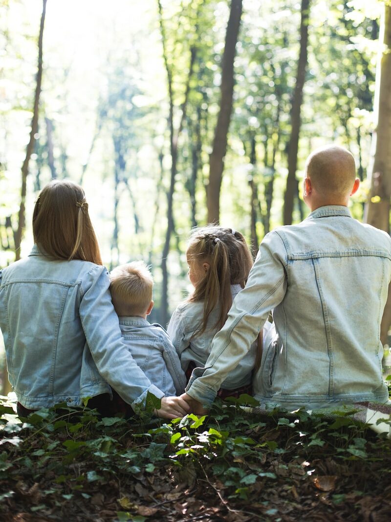 man and woman holding hands together with boy and girl looking at green trees during day