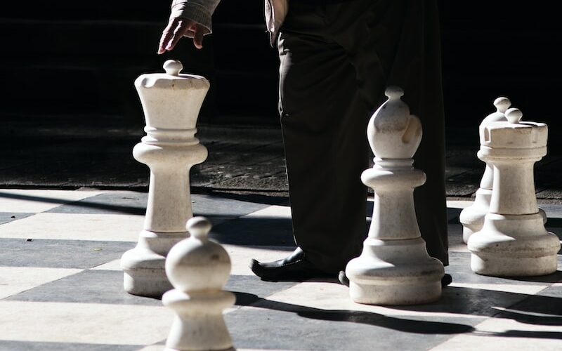 man in black and white jacket and black pants standing beside white chess piece